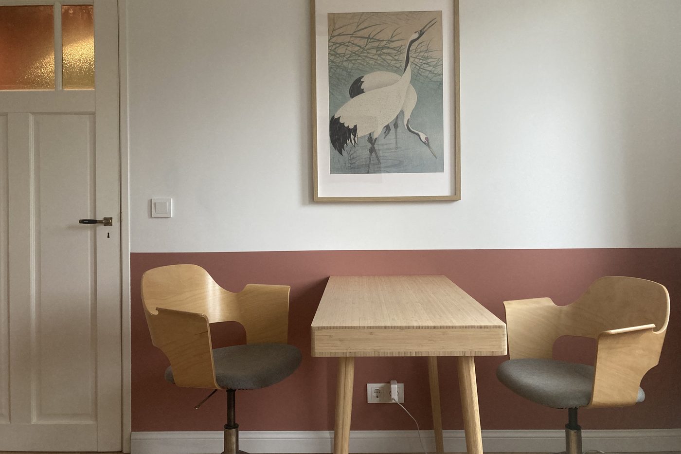 De overlegtafel in de praktijk met twee stoelen tegenover elkaar, onder een prent van kraanvogels